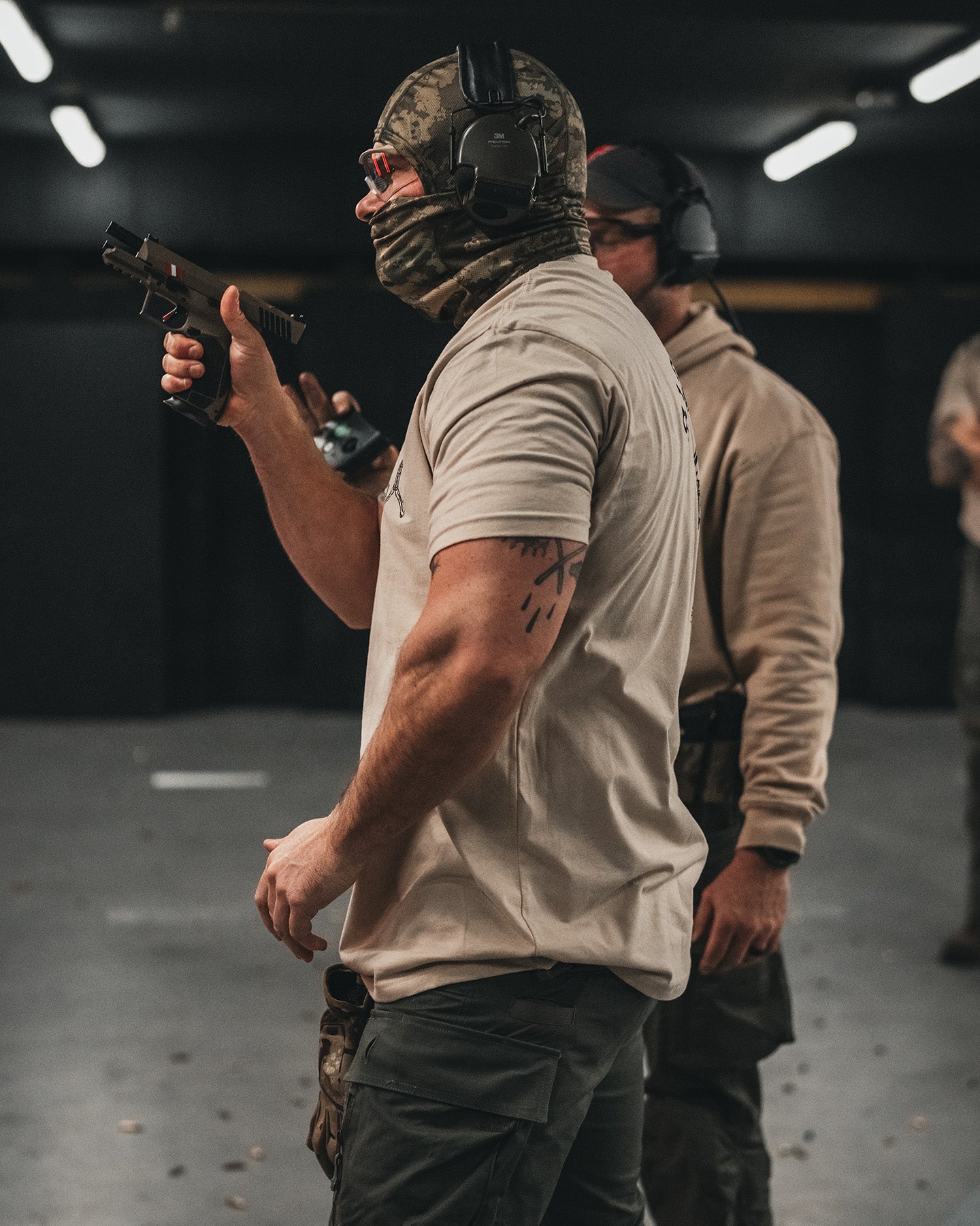Shooter in the sand Stay Violent T-Shirt firing a pistol at an indoor range #color_sand #in_field