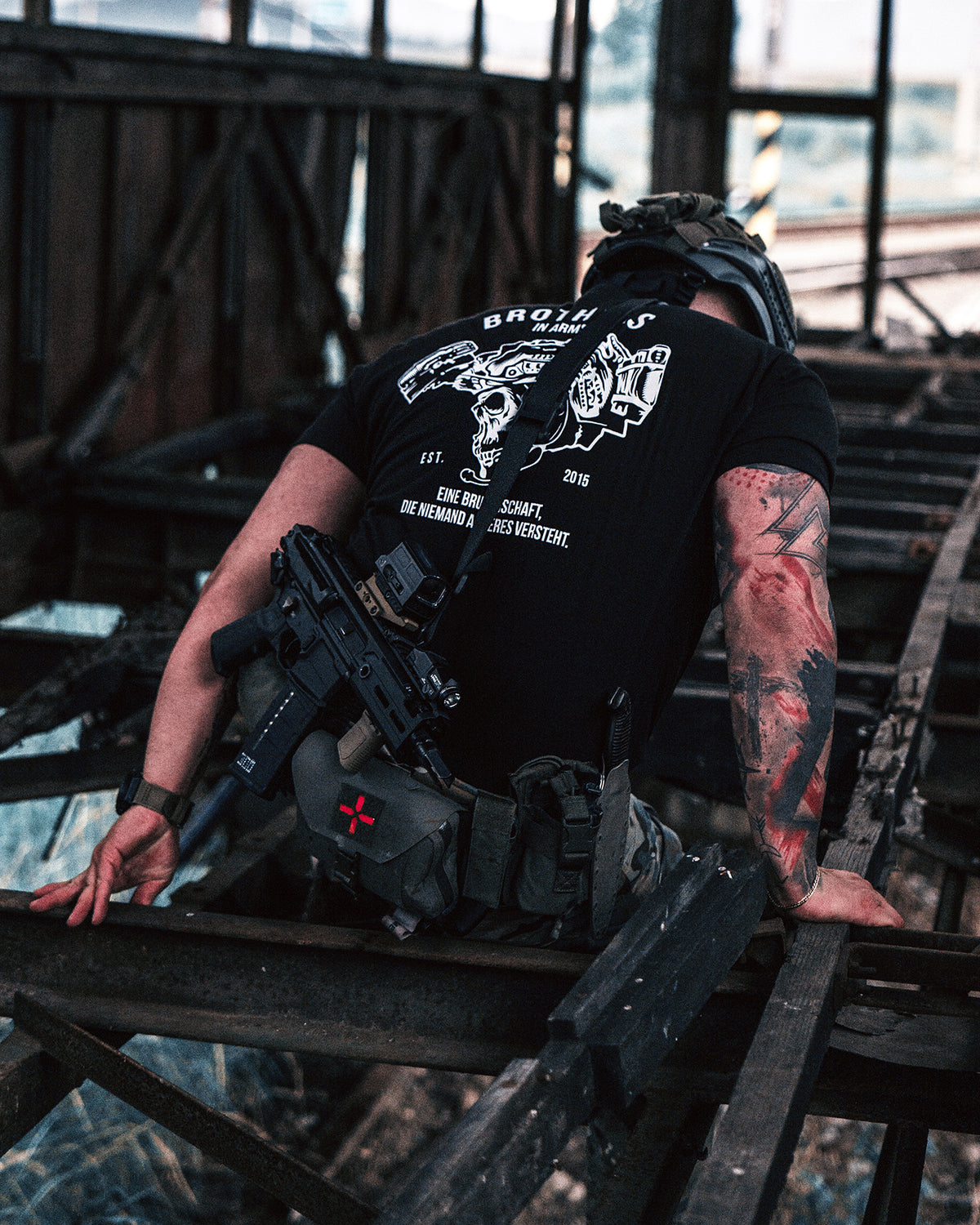 Man with a rifle climbing through an abandoned building, wearing the black Team T-Shirt