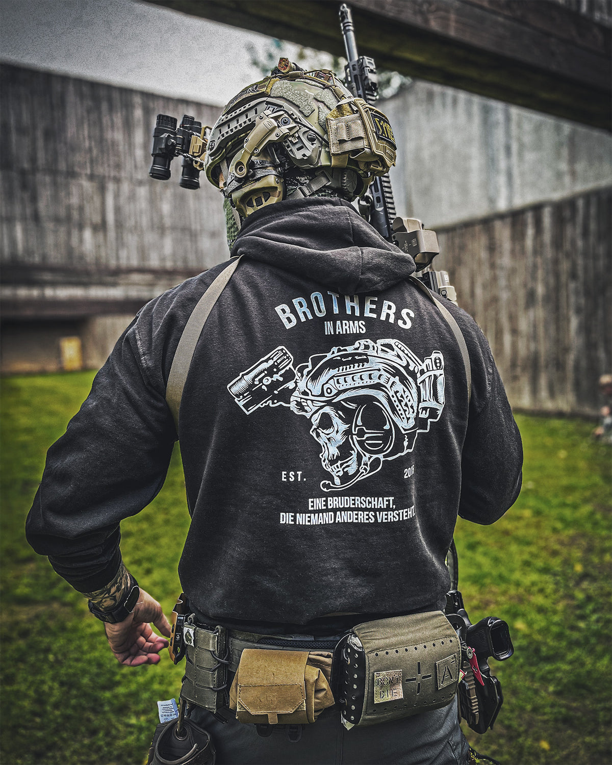 Man from behind in the black Team Hoodie with helmet and rifle outdoors