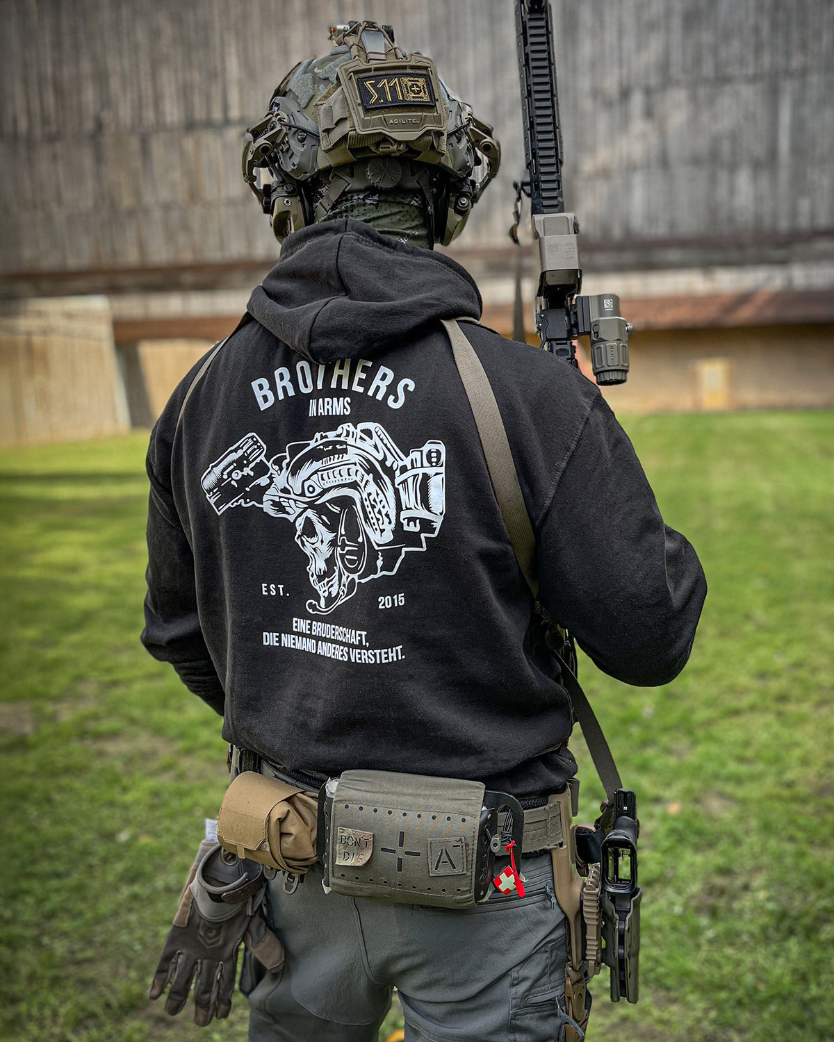 Man from behind in the black Team Hoodie with a rifle on a training ground