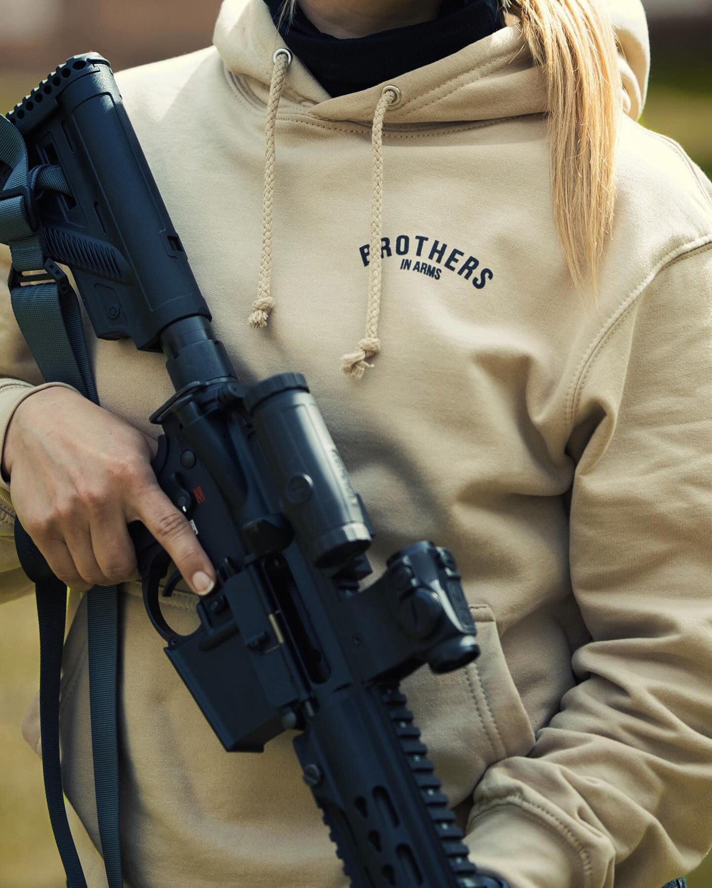Woman with a rifle wearing the sand Team Hoodie, front view with chest print #color_sand #in_field