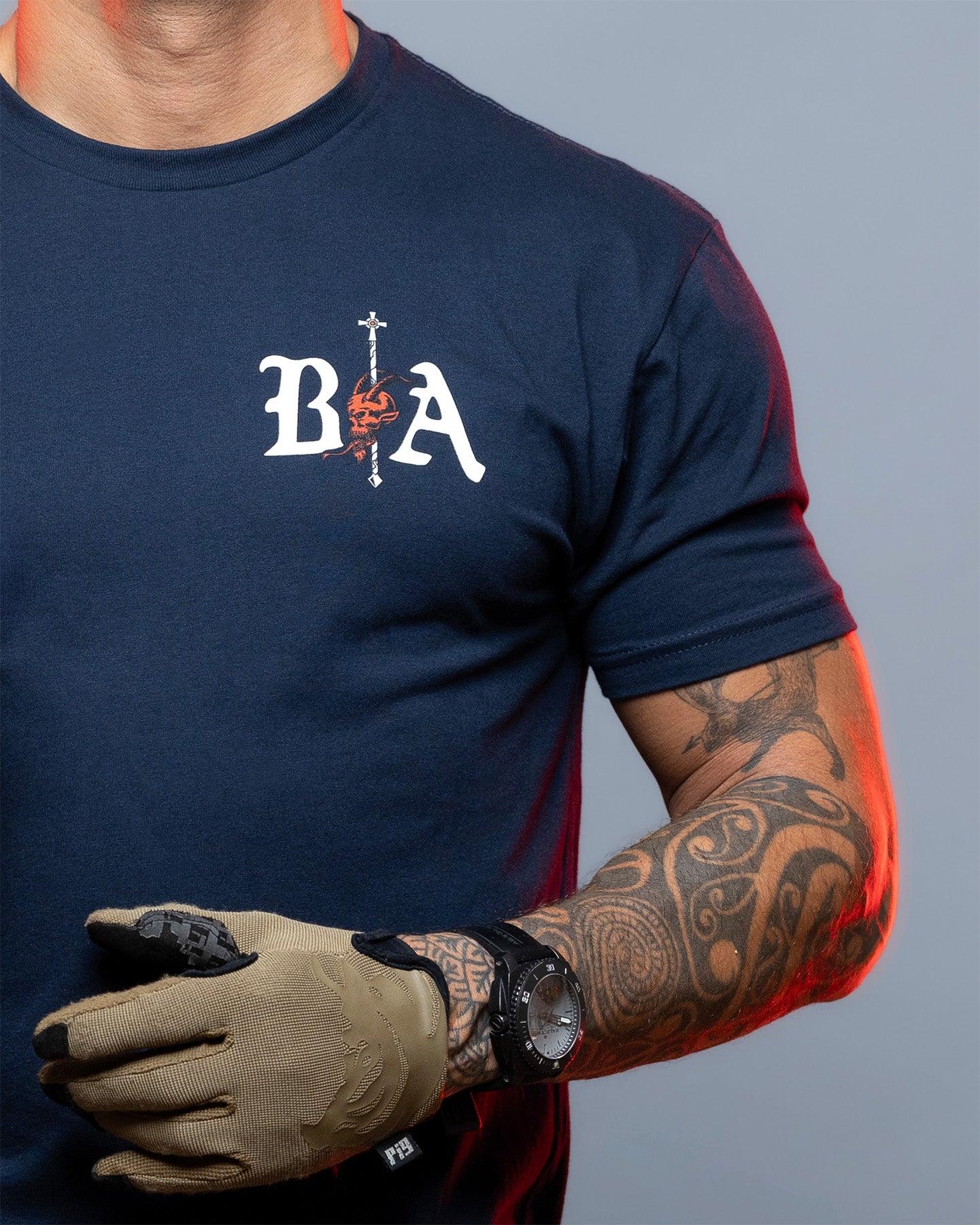Person wearing a navy blue t-shirt with 'BA' logo, holding a glove against a gray background. #color_navy