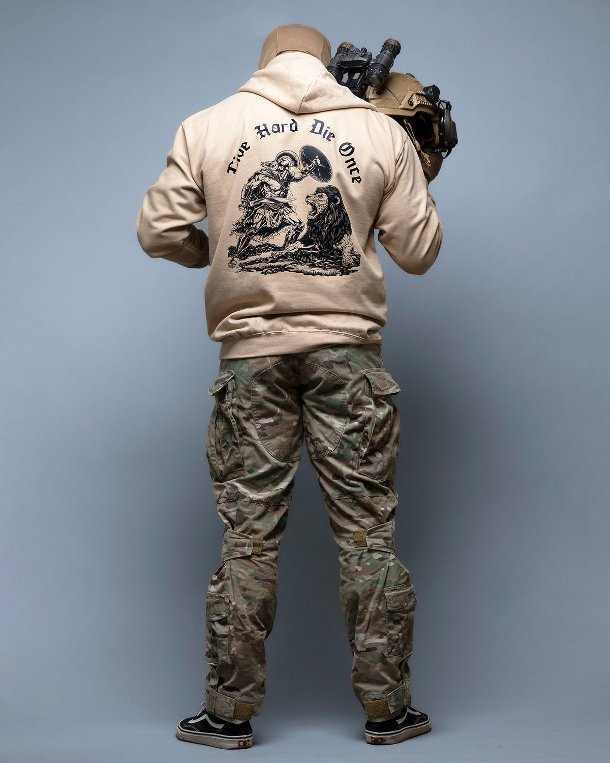 Full-length shot of the sand Live Hard Die Once Hoodie from behind, worn with camo trousers