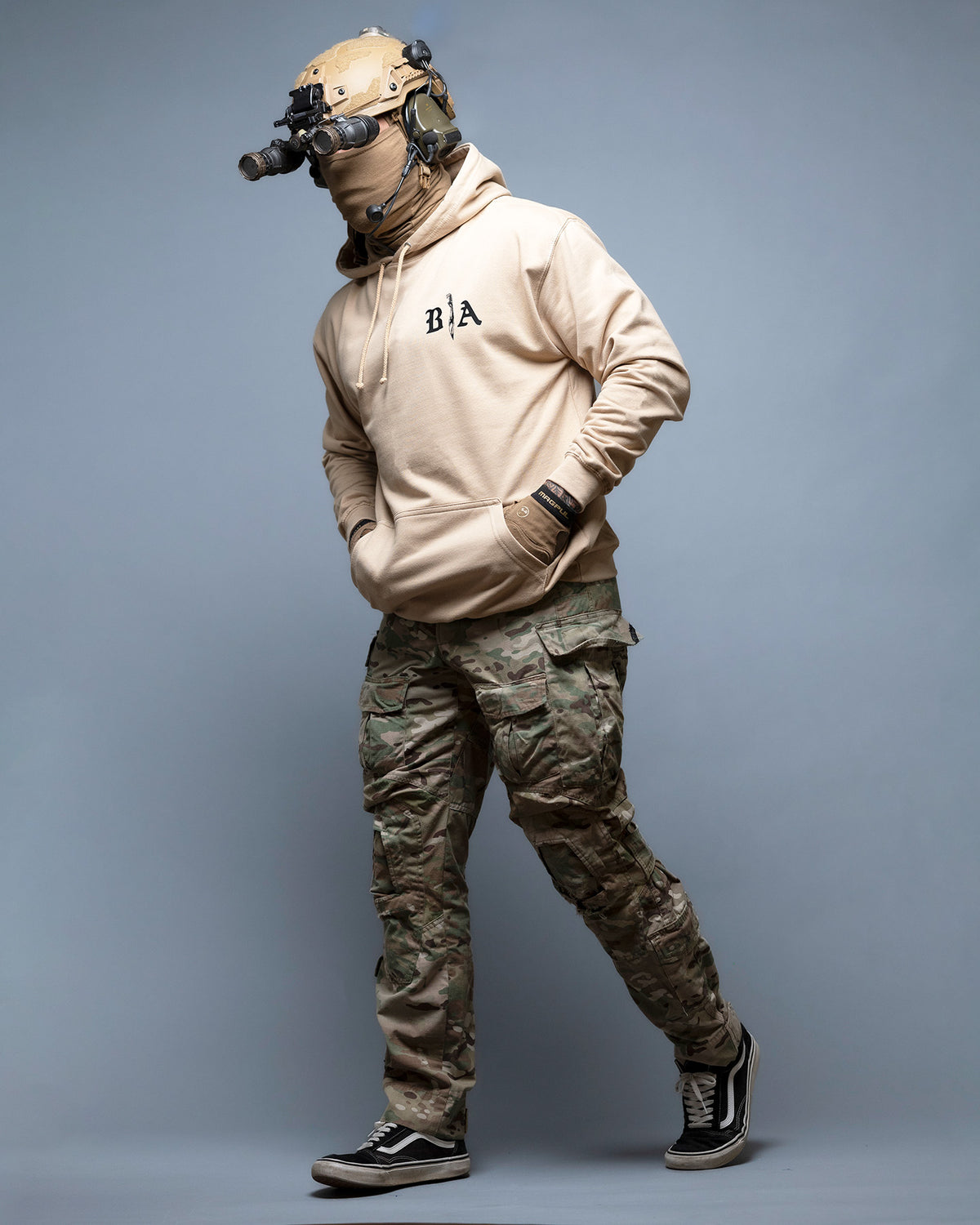 Full-length shot of the sand Live Hard Die Once Hoodie worn with camo trousers and a helmet