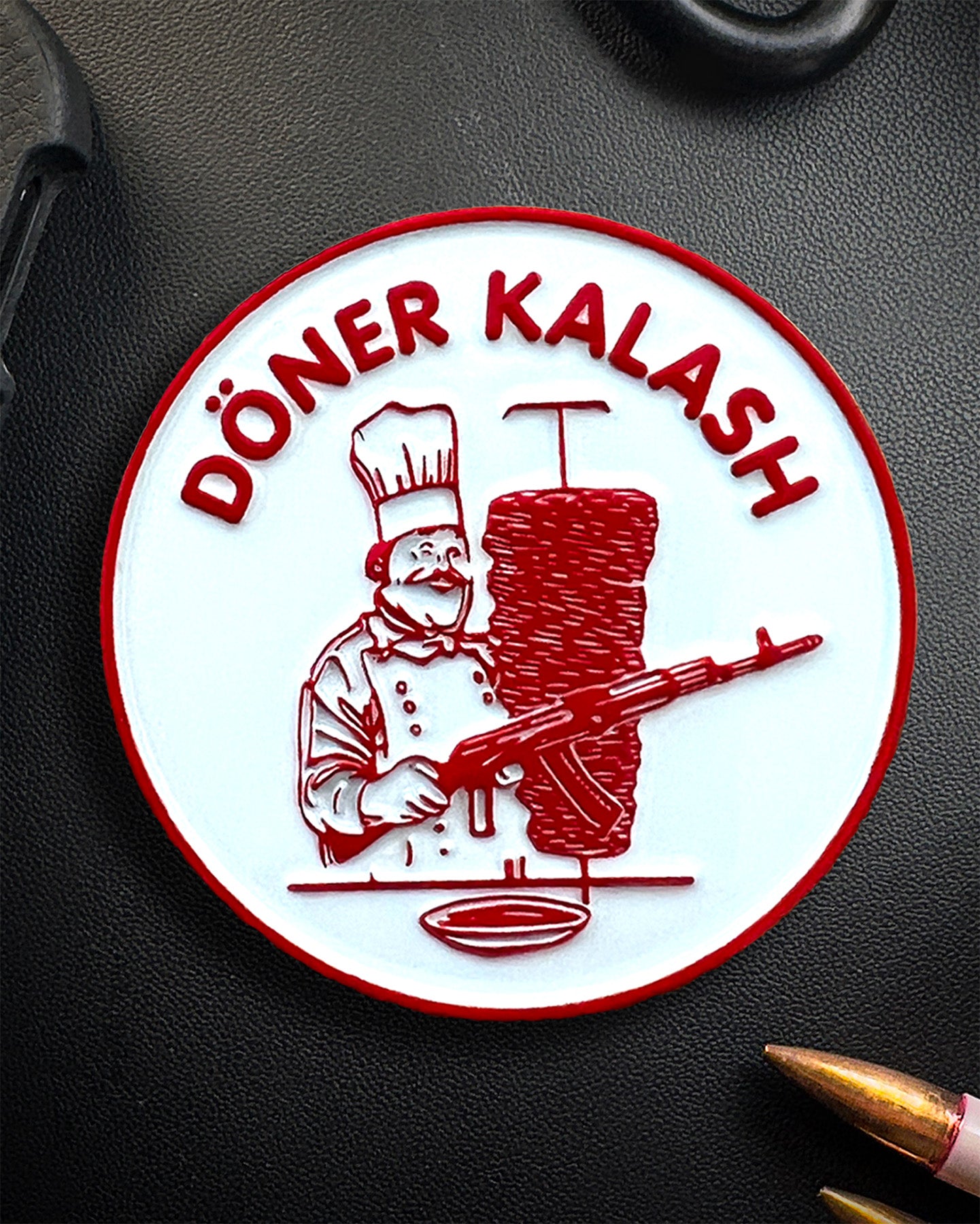 Circular Coin with a Döner Kebab chef and rifle on a dark surface, with the text "Döner Kalash"