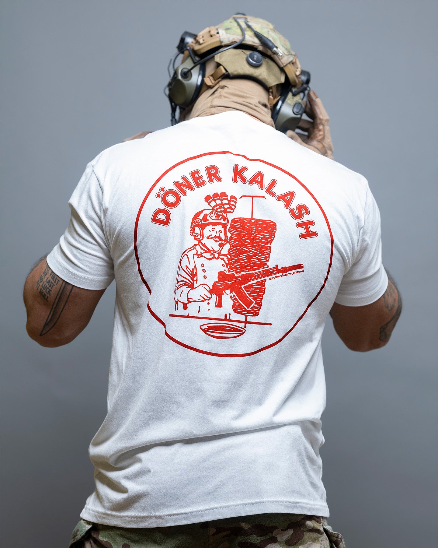 Person wearing a white t-shirt with red graphic and text on the back, standing against a gray background. #color_white