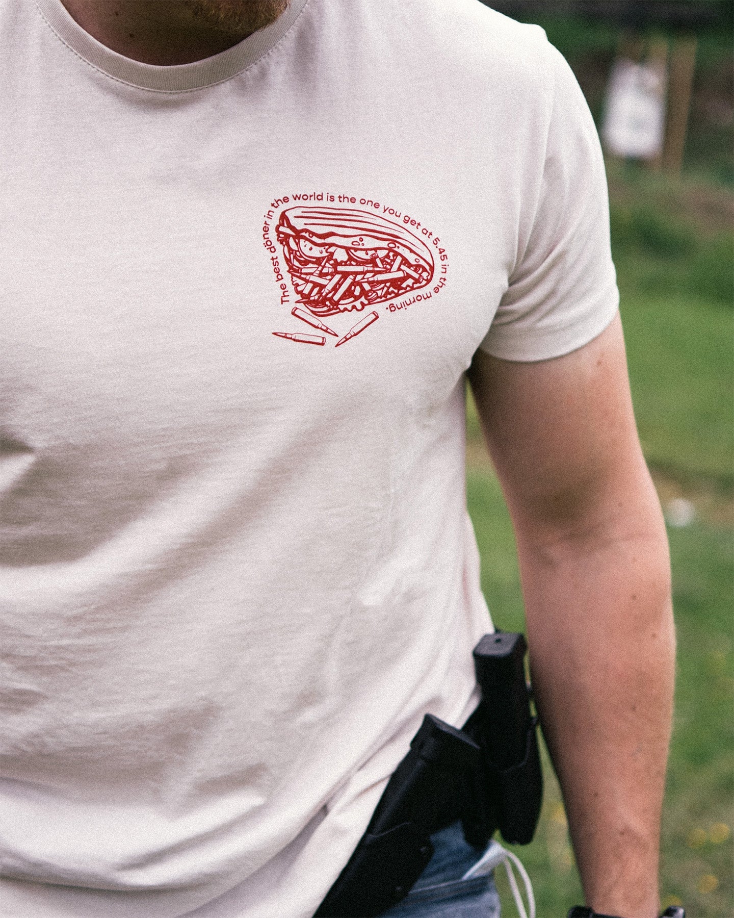 Person wearing a white t-shirt with a red graphic design on a grassy background. #color_white #in_field