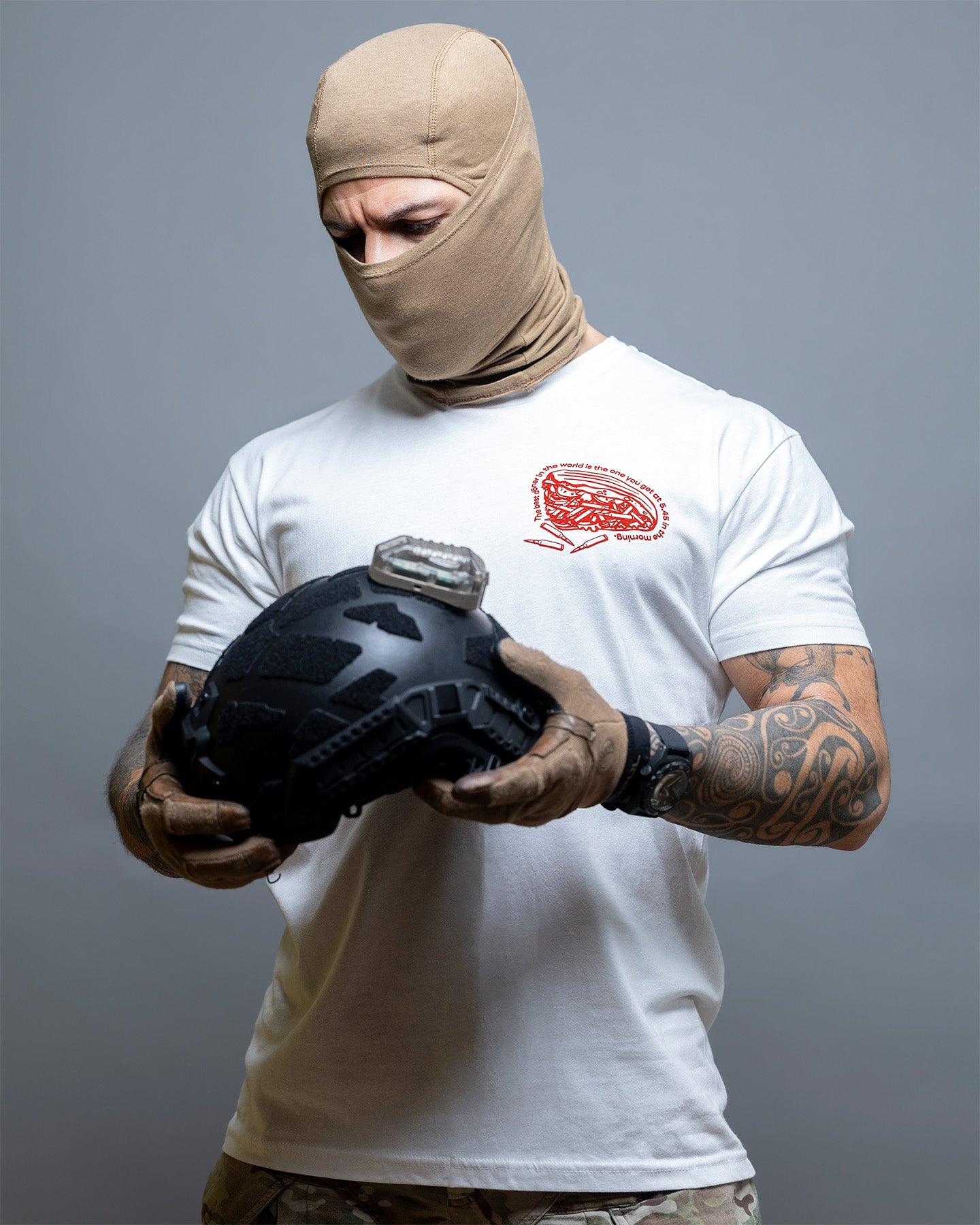 Person wearing a white t-shirt with a logo, holding a black helmet against a gray background. #color_white
