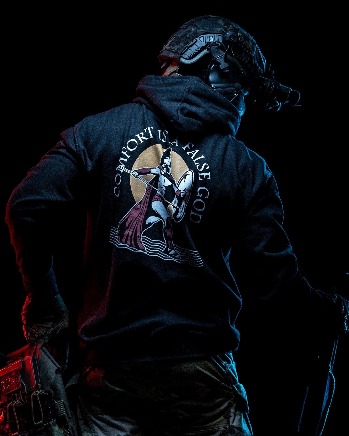 Man from behind in the black Comfort Is A False God Hoodie with a helmet in blue light #color_black #in_field