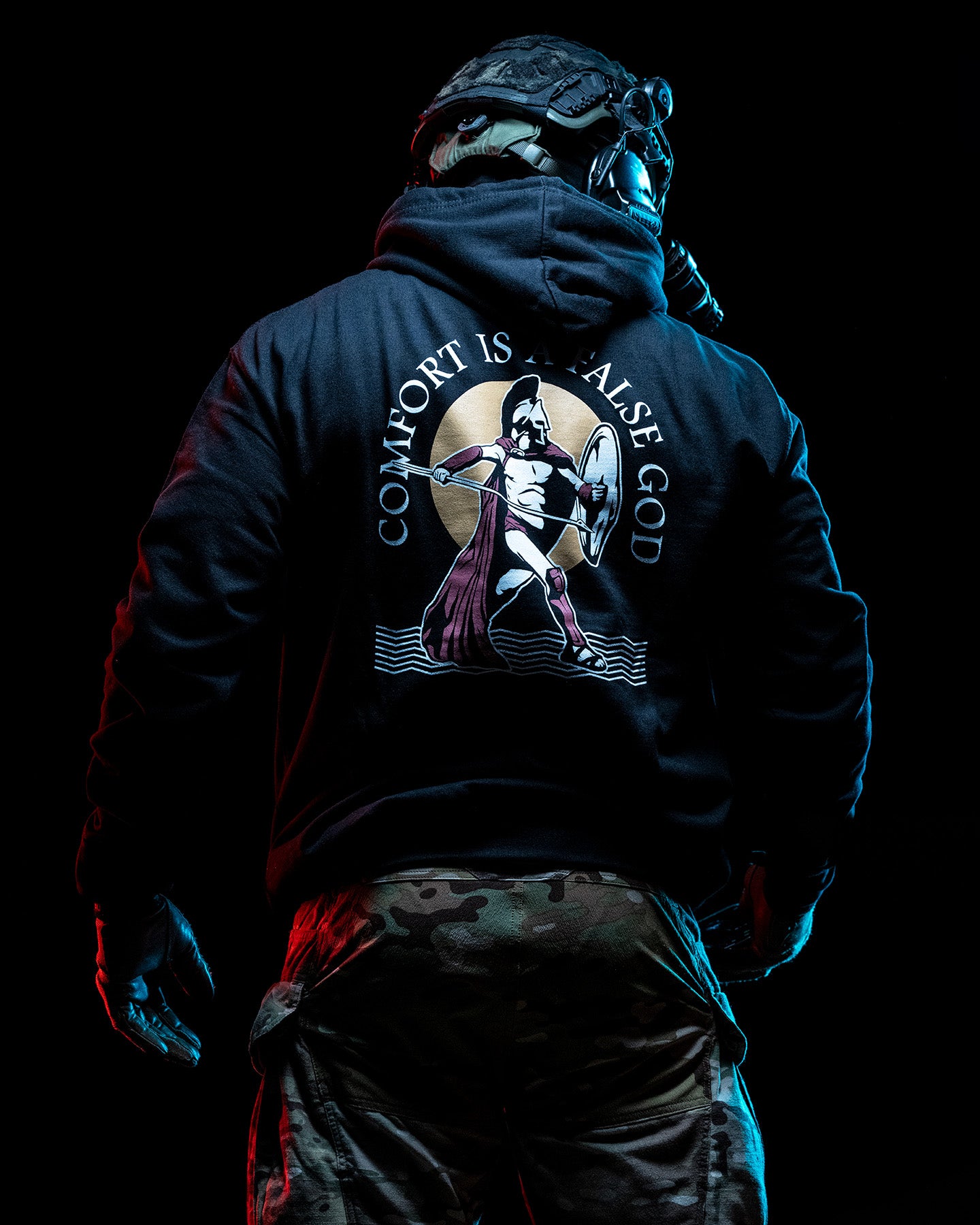 Man from behind in the black Comfort Is A False God Hoodie, hood up with a neck gaiter #color_black #in_field