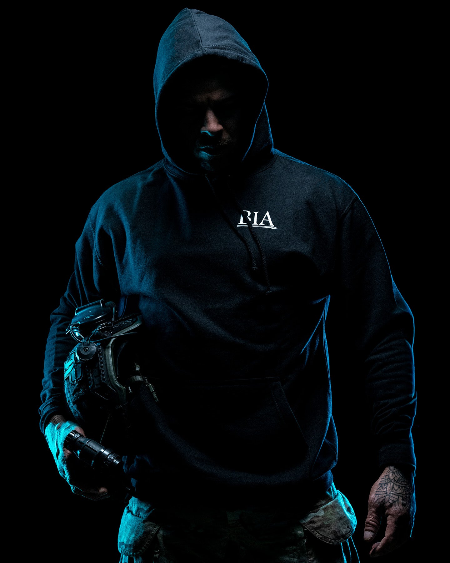 Man in the black Comfort Is A False God Hoodie with the hood up in blue light #color_black #in_field