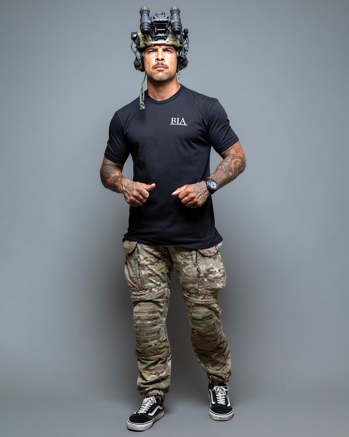 Full-length shot of the black Comfort Is A False God T-Shirt worn with camo trousers
