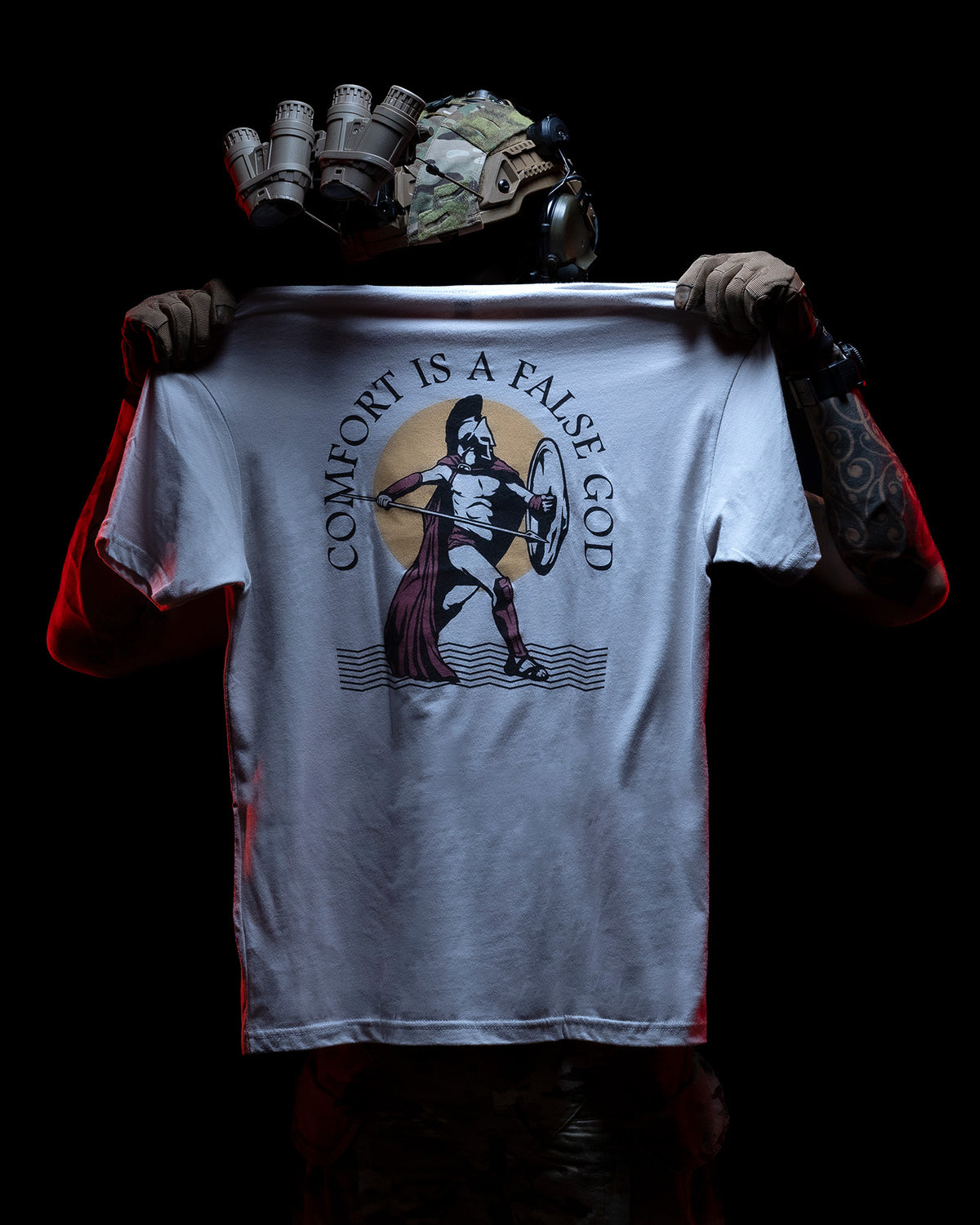 Man holding open the gray Comfort Is A False God T-Shirt to show the Spartan back print