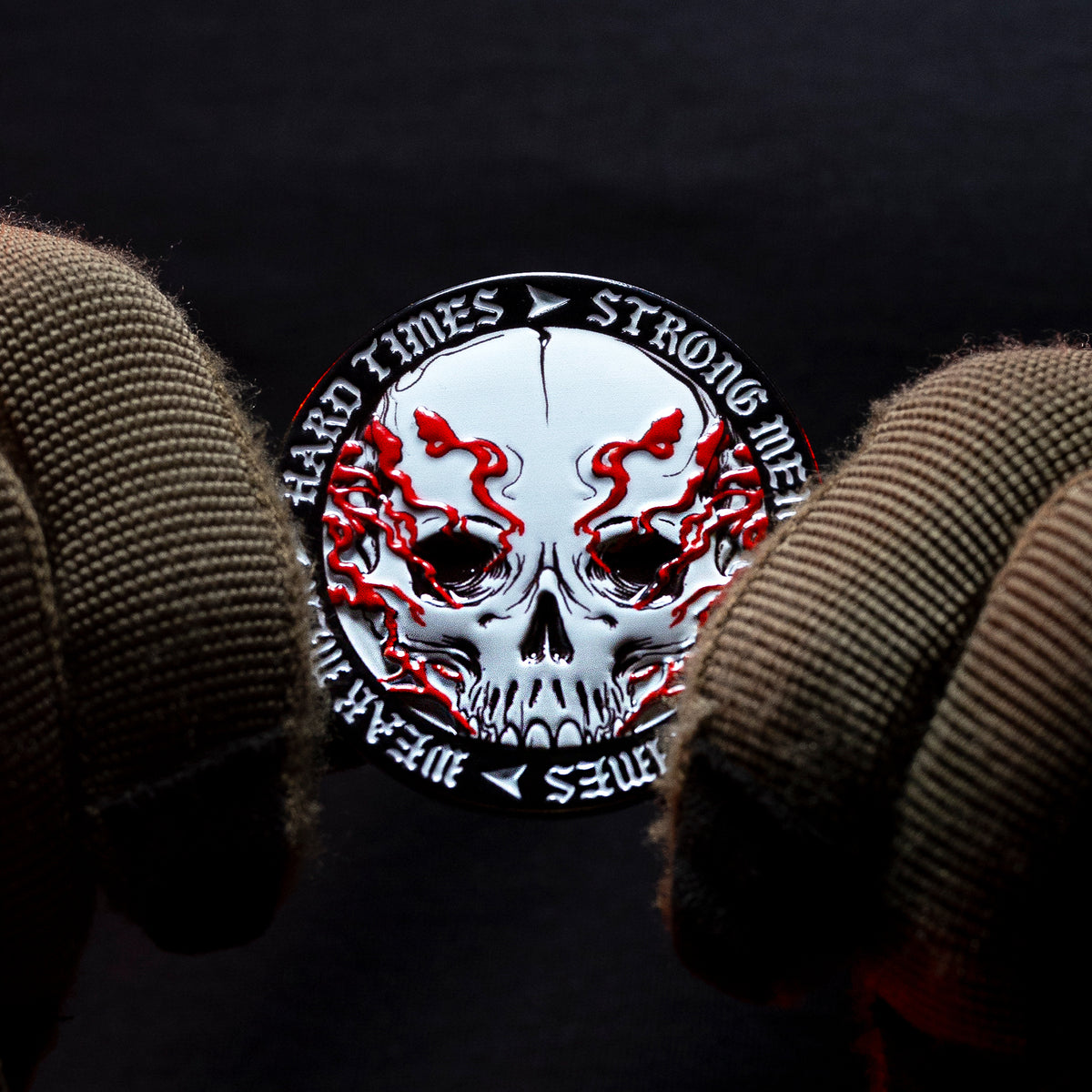 Gloved hand holding the Hard Times coin, skull side with the lettering around the edge