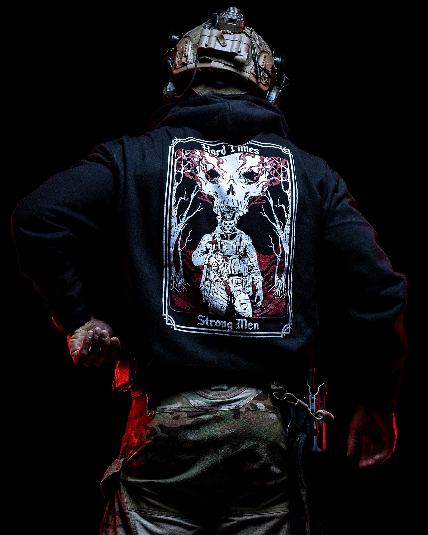 Man from behind in the black Hard Times Hoodie with camo trousers in low light #color_black #in_field