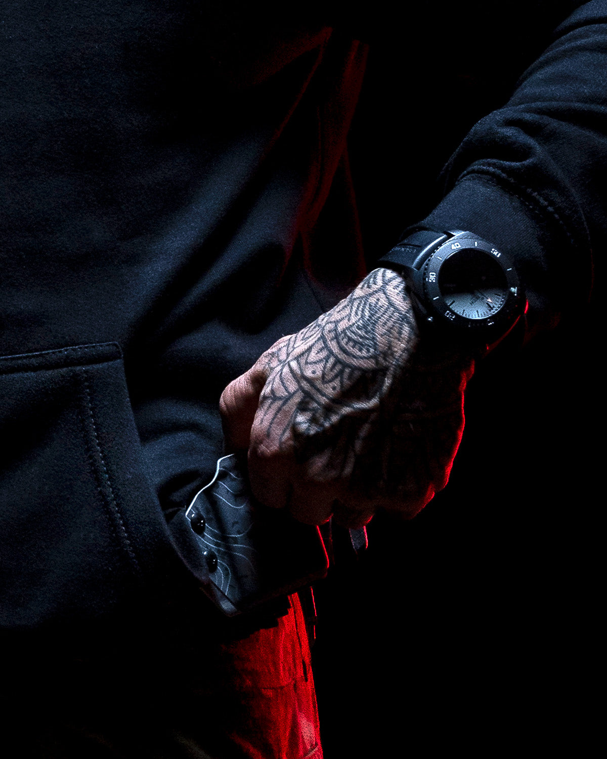 Gloved hand holding a flashlight next to the black Hard Times Hoodie in red light #color_black #in_field