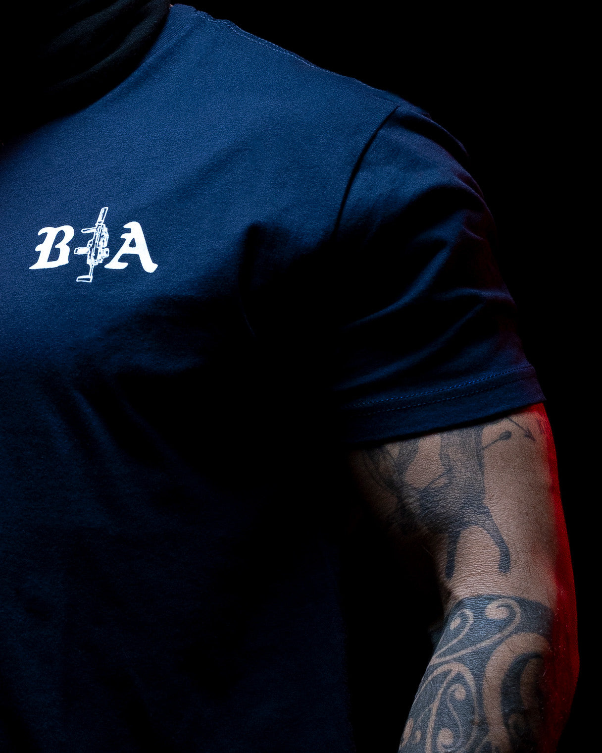 Close-up of the B|A chest logo on the navy Hard Times T-Shirt in low light #color_navy #in_field