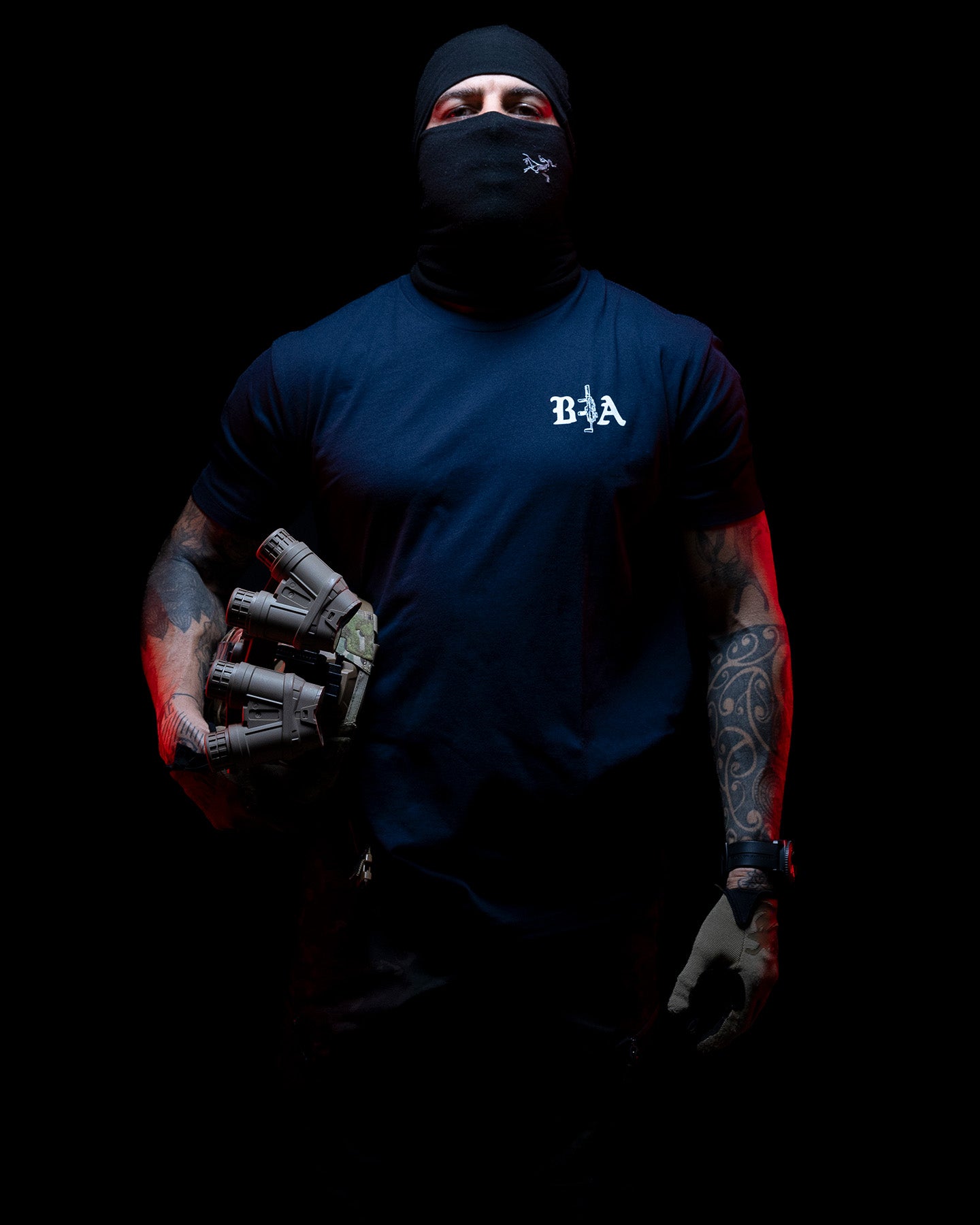 Man in a balaclava wearing the navy Hard Times T-Shirt against a dark background #color_navy #in_field