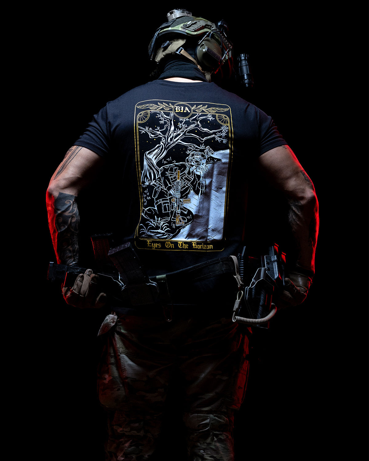 Man from behind in the black Eyes On The Horizon T-Shirt with a plate carrier in the dark