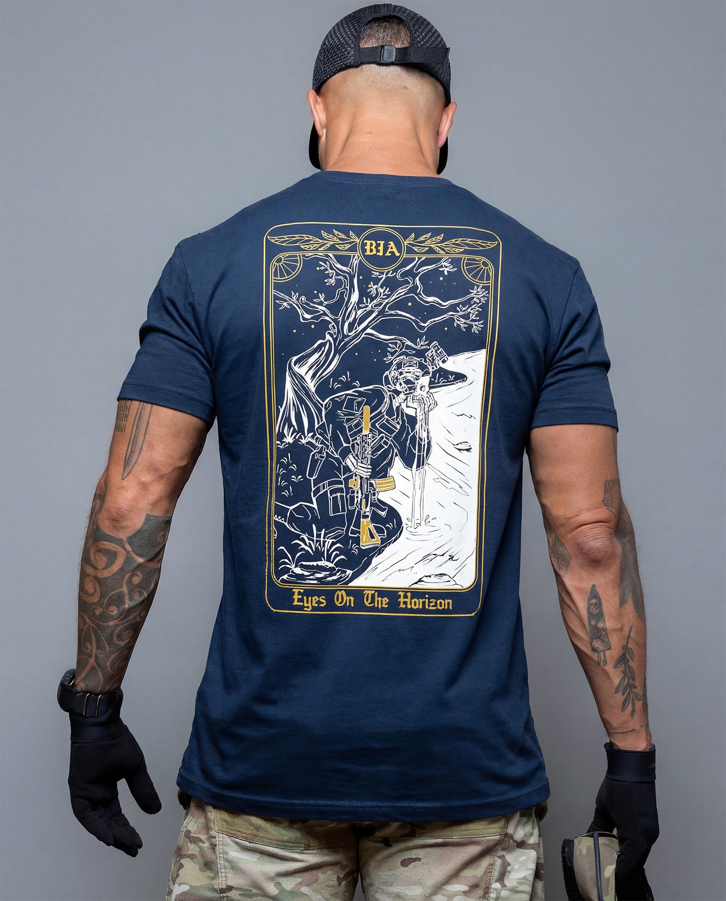 Man wearing a navy blue t-shirt with a graphic design on the back, standing against a gray background. #color_navy