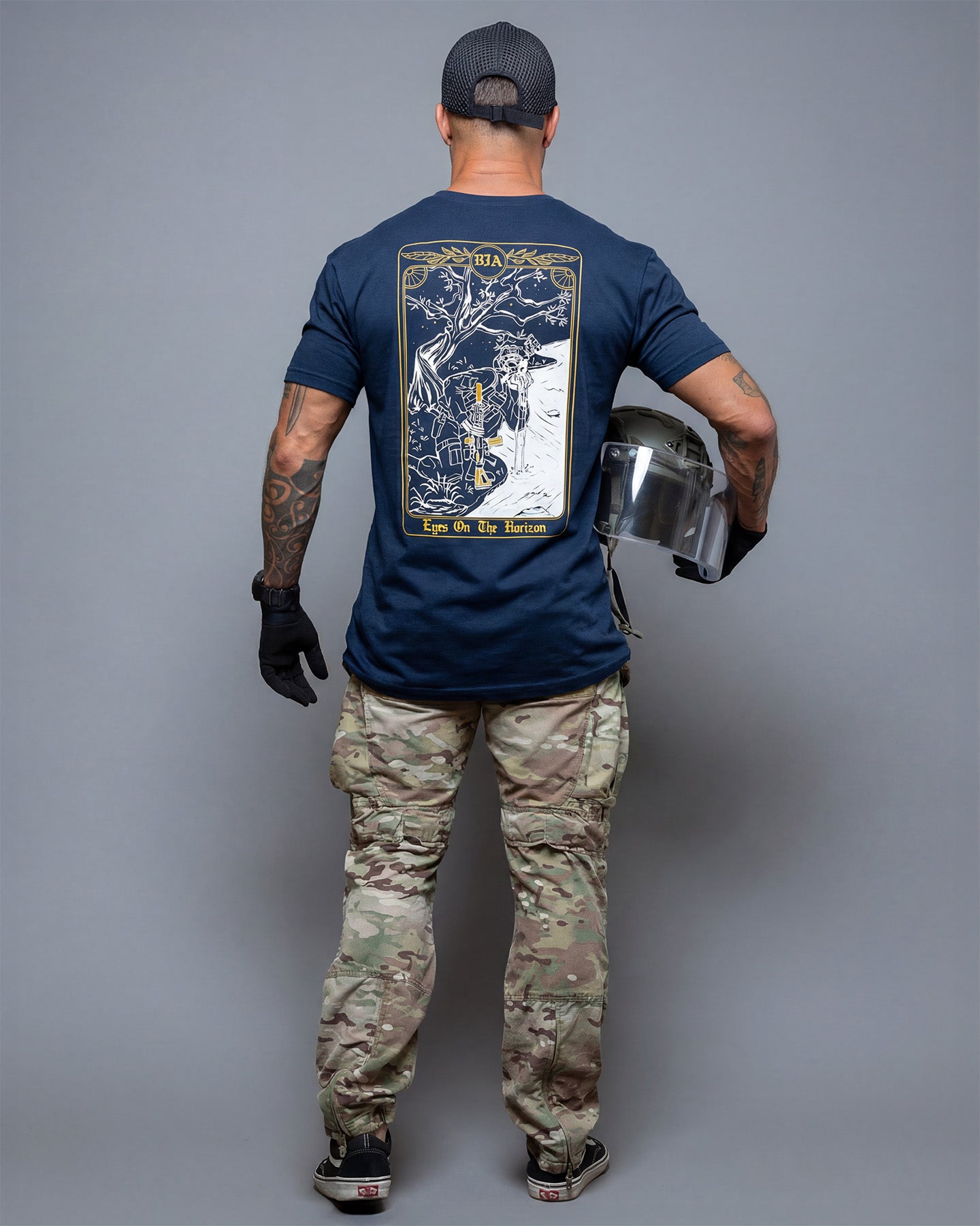 Person wearing a navy blue t-shirt with a graphic design, holding a helmet, on a gray background. #color_navy