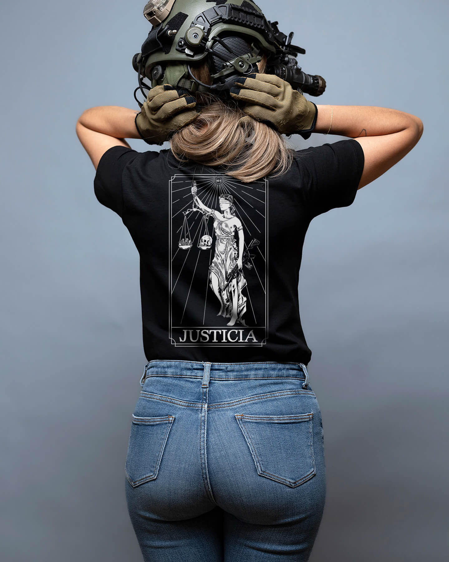 Person wearing a black t-shirt with 'JUSTICIA' design and blue jeans, standing against a gray background. #color_black
