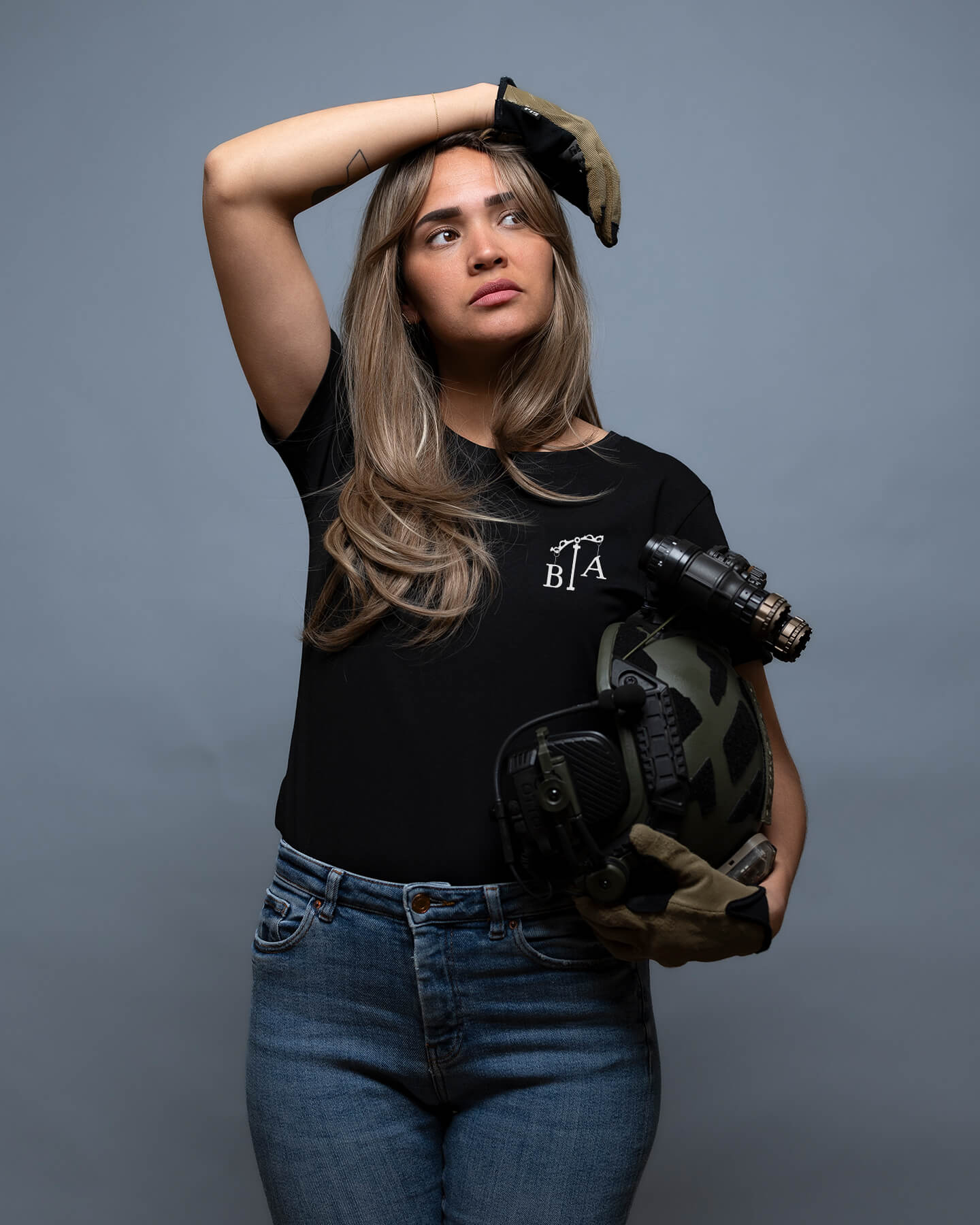 Person wearing a black t-shirt with a logo, holding a helmet and gloves against a gray background. #color_black