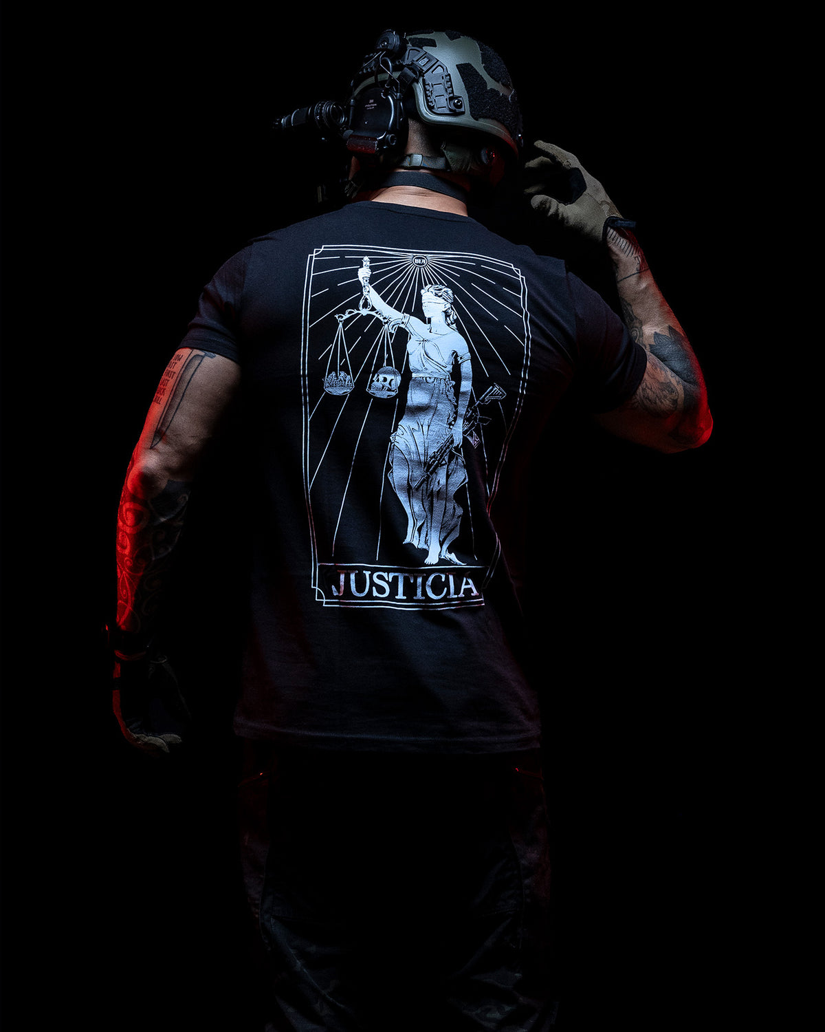 Man from behind in the black Justicia T-Shirt with a helmet, lit red in the dark