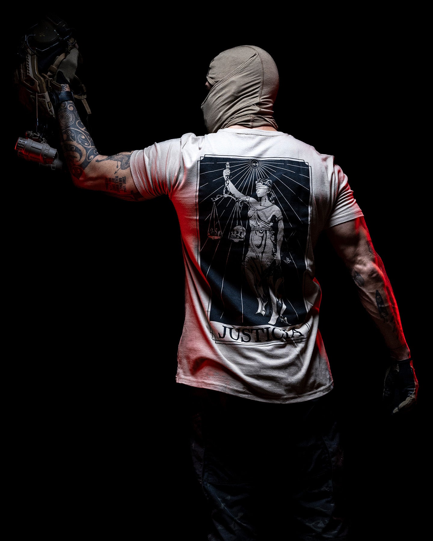 Man in a balaclava wearing the sand Justicia T-Shirt, seen from behind in red light #color_sand #in_field