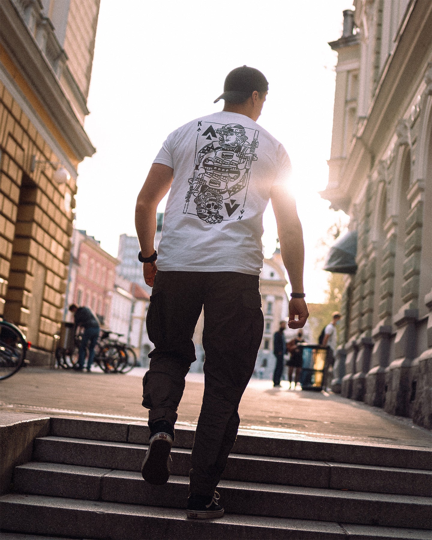 Man from behind walking up steps in a city street, wearing the white King of Spades T-Shirt #color_white #in_field