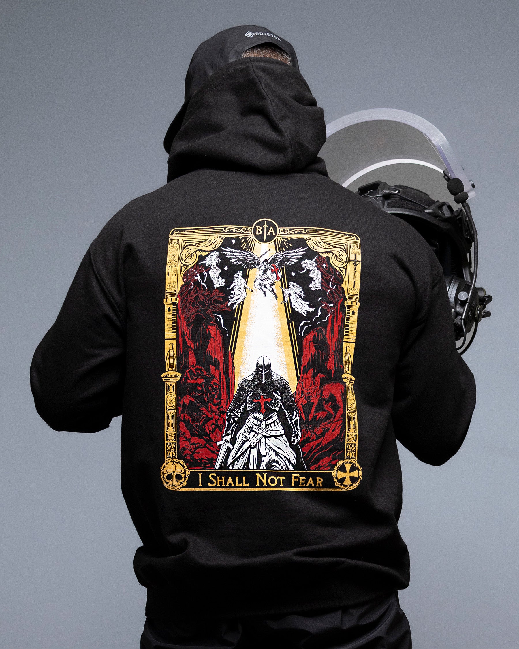 Person wearing a black hoodie with a graphic design on the back, standing against a gray background. #color_black
