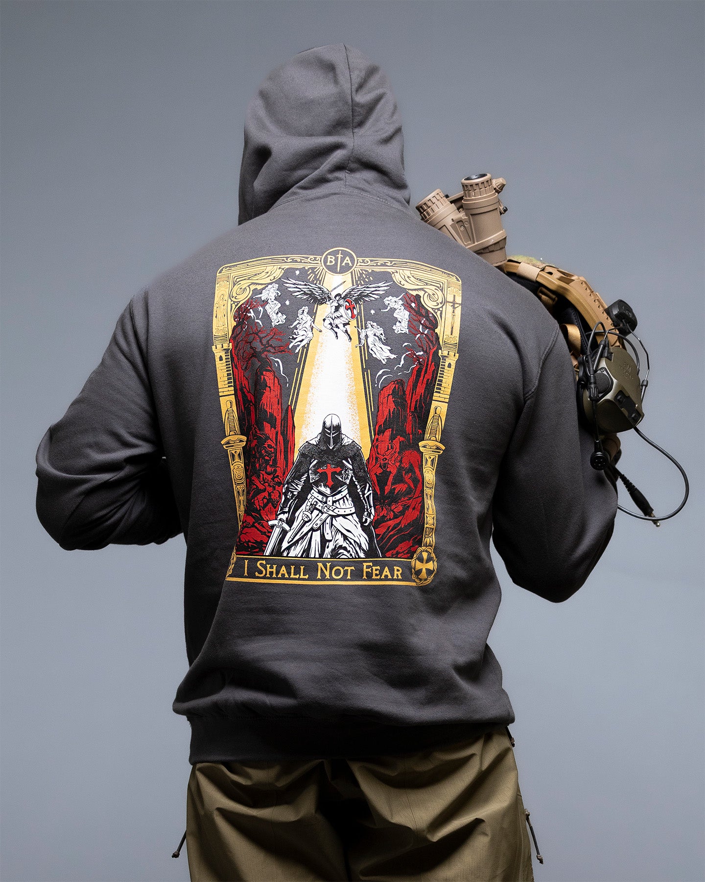 Person wearing a dark hoodie with a graphic design on the back against a gray background. #color_steel grey
