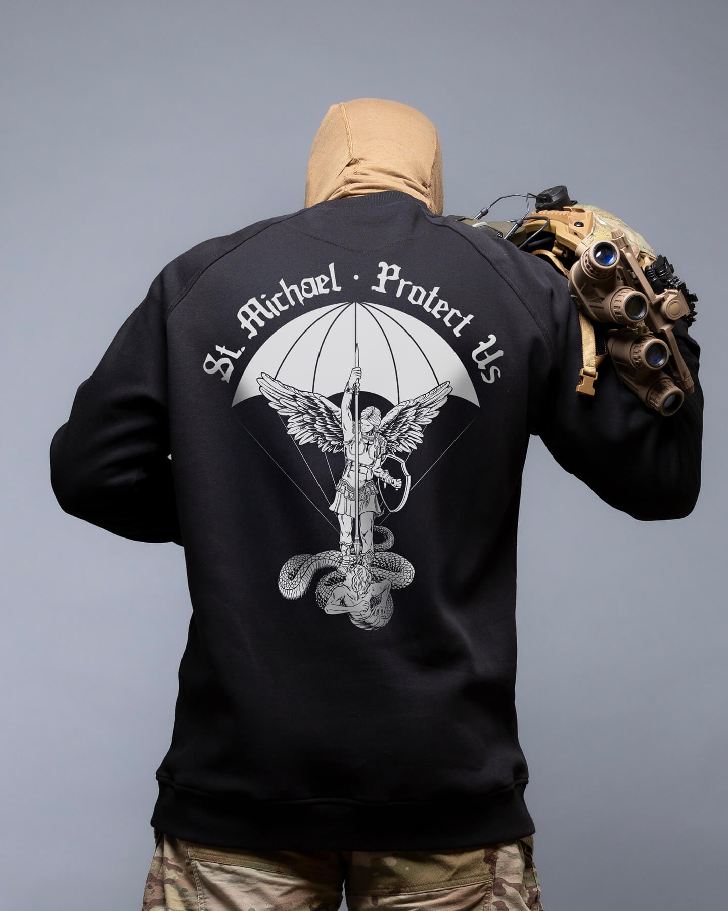 Person wearing a black jacket with 'St. Michael Protect Us' design on the back, holding a helmet. #color_black