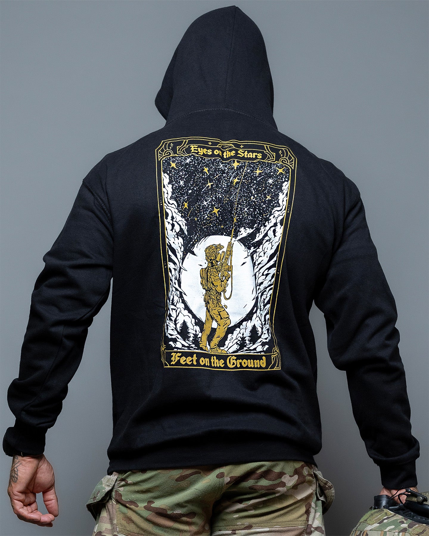 Black hoodie with a graphic design on the back, worn by a person against a gray background. #color_black