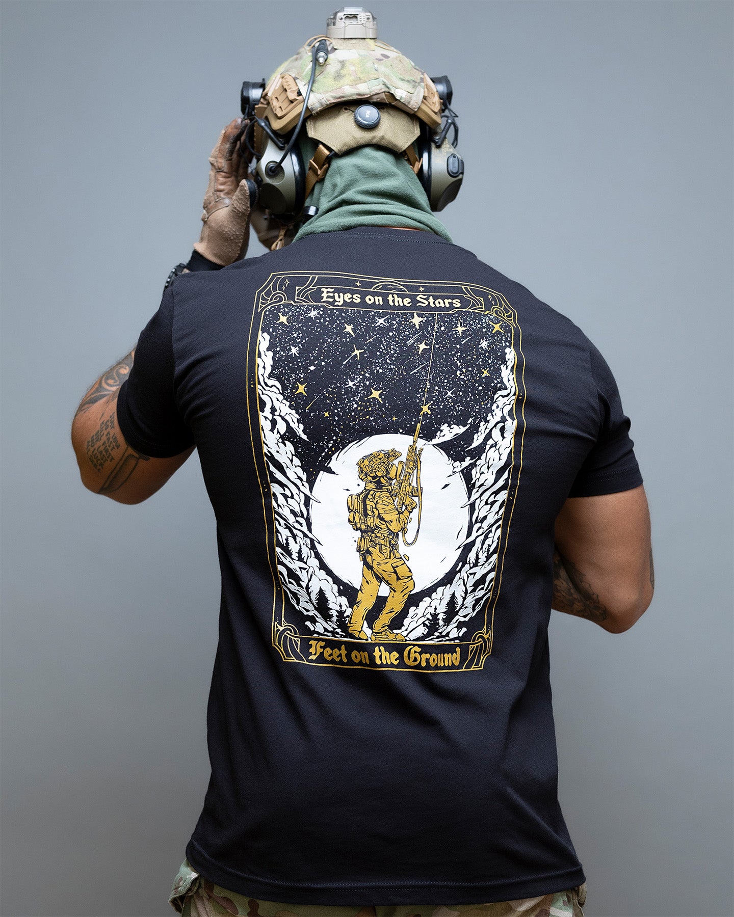 Person wearing a black t-shirt with a graphic design on the back, standing against a gray background. #color_black