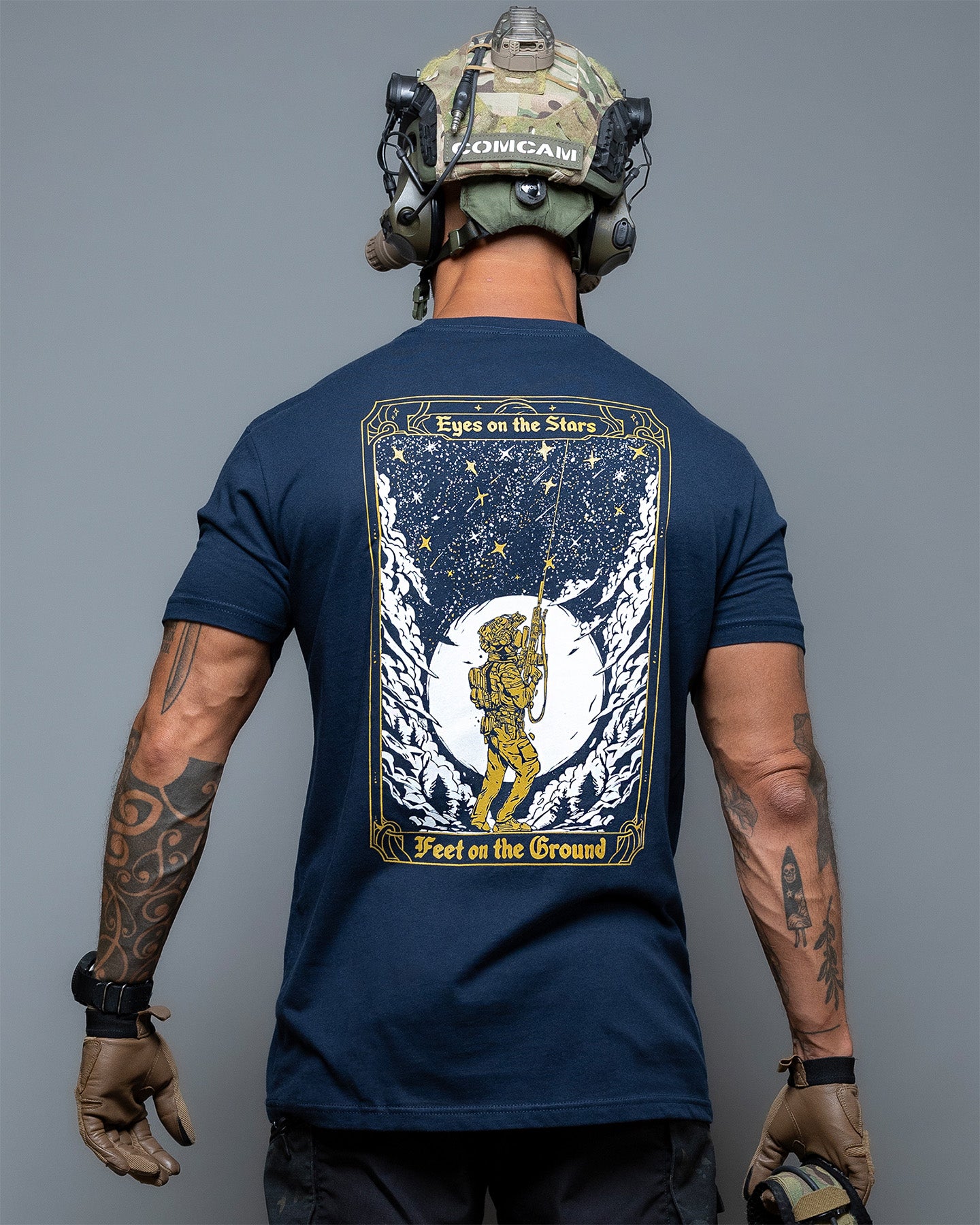 Person wearing a navy blue t-shirt with a graphic design on the back, standing against a gray background. #color_navy