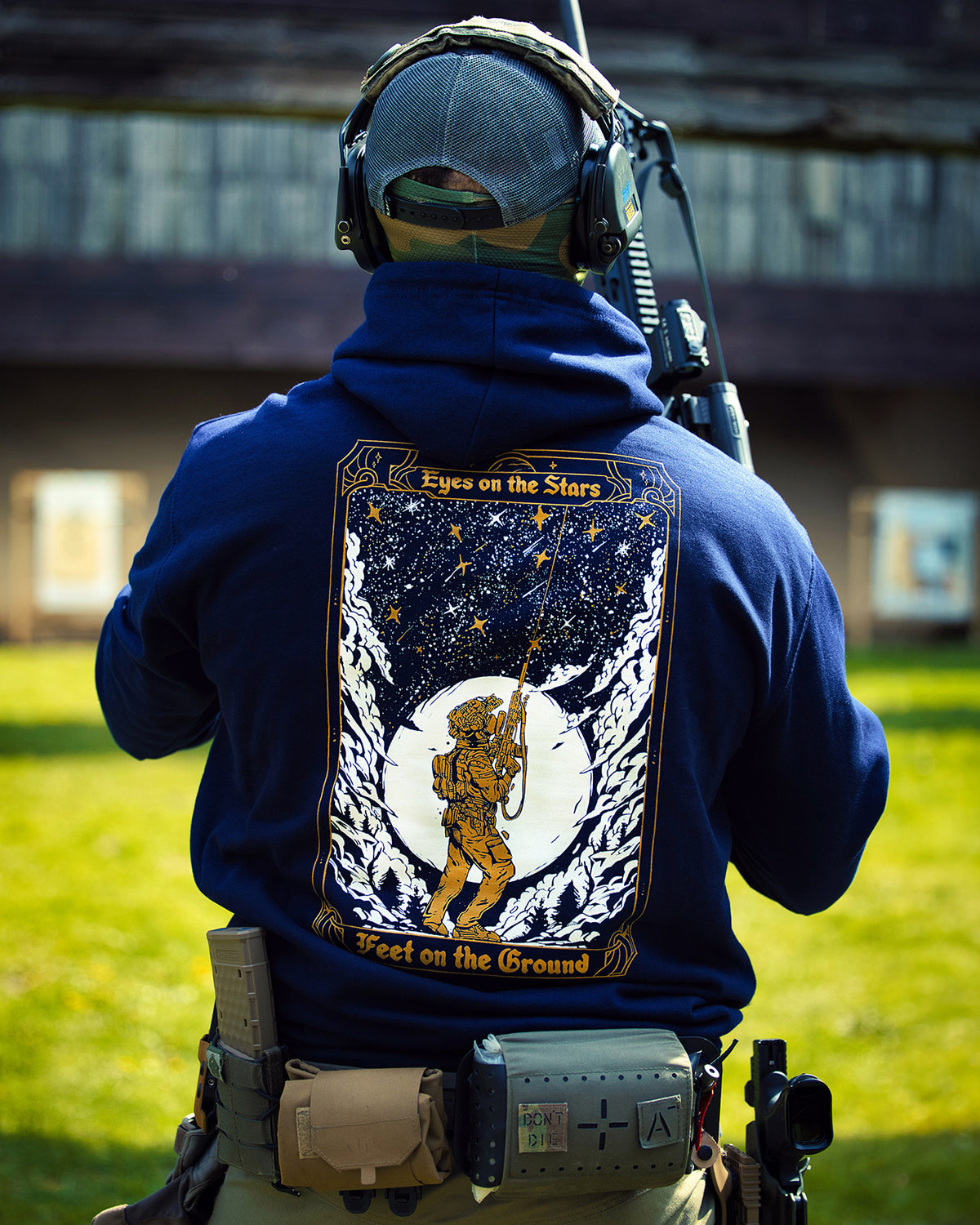 Man from behind in the navy Eyes On The Stars Hoodie with a rifle, tarot card back print