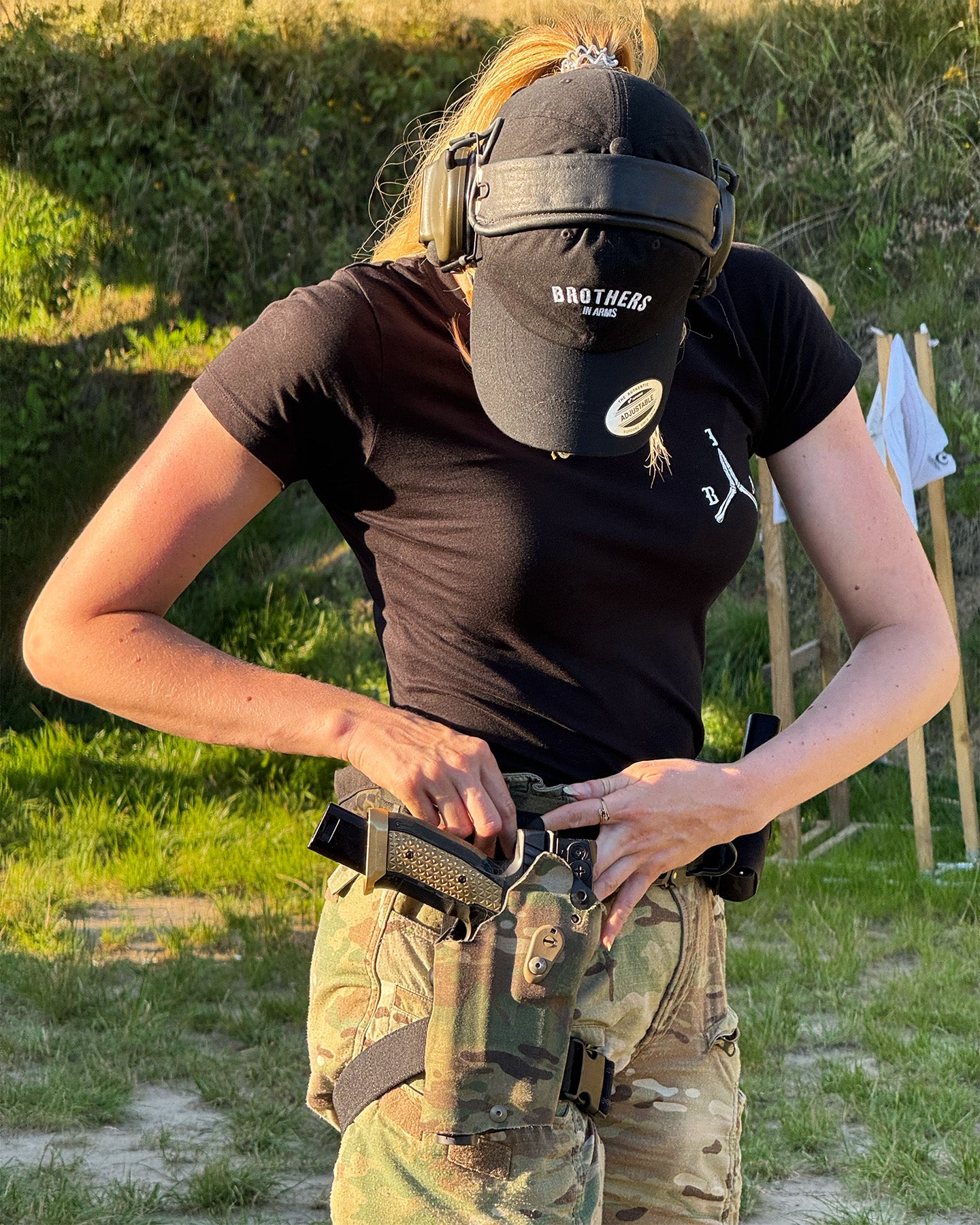 Person wearing tactical gear with a gun in a grassy outdoor area.  #color_black #in_field