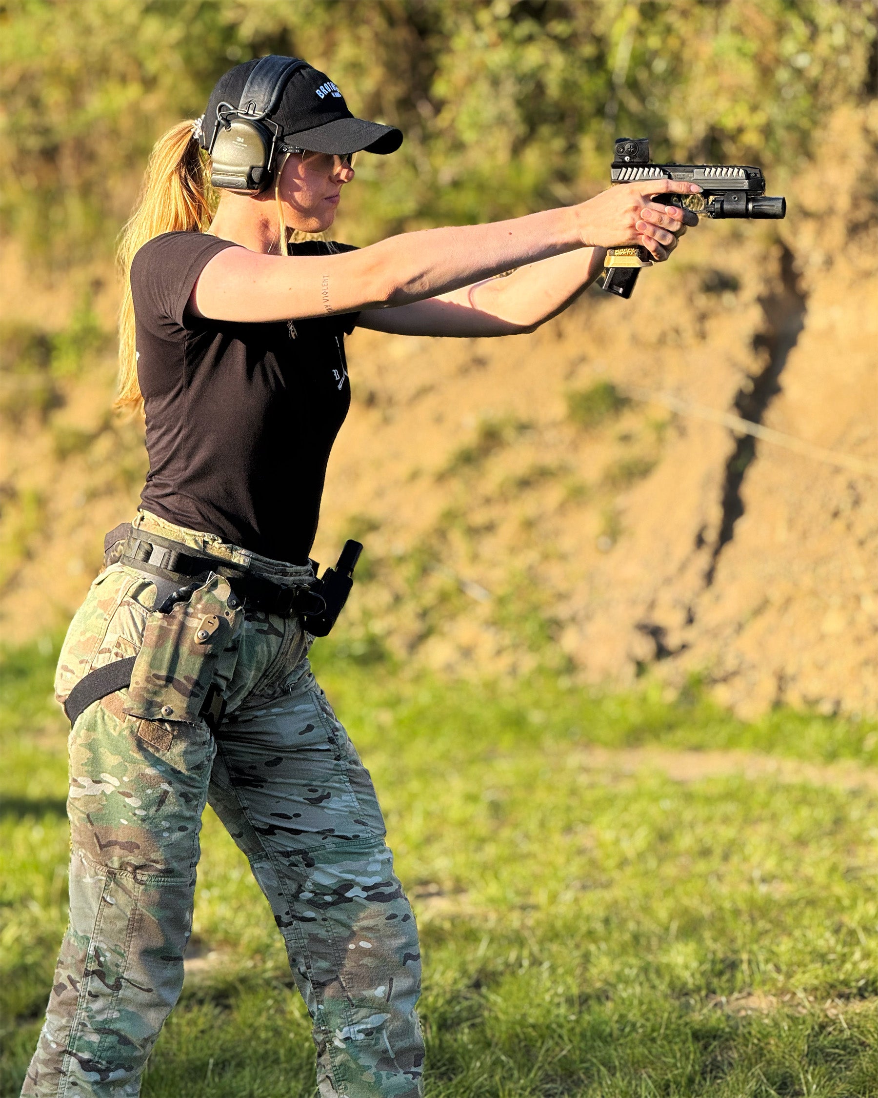 Person in tactical gear holding a handgun outdoors.  #color_black #in_field